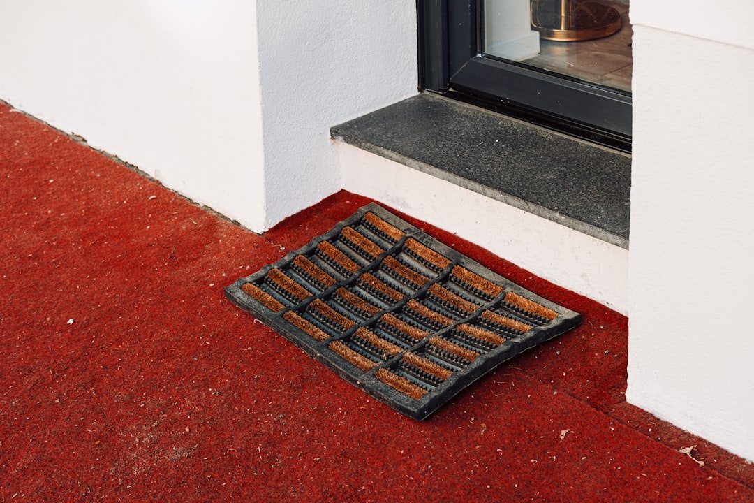 A doormat sits on a red floor by a door.